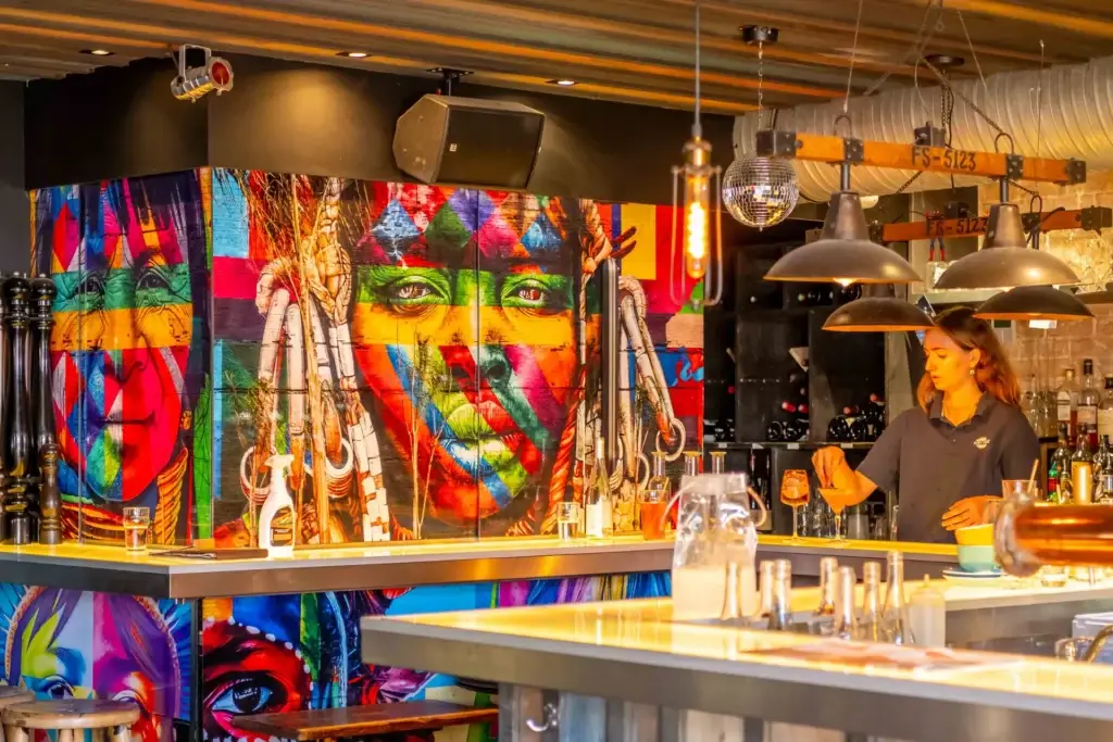 Bar de Chez Pont-Pont avec grande fresque colorée et serveuse derrière le comptoir