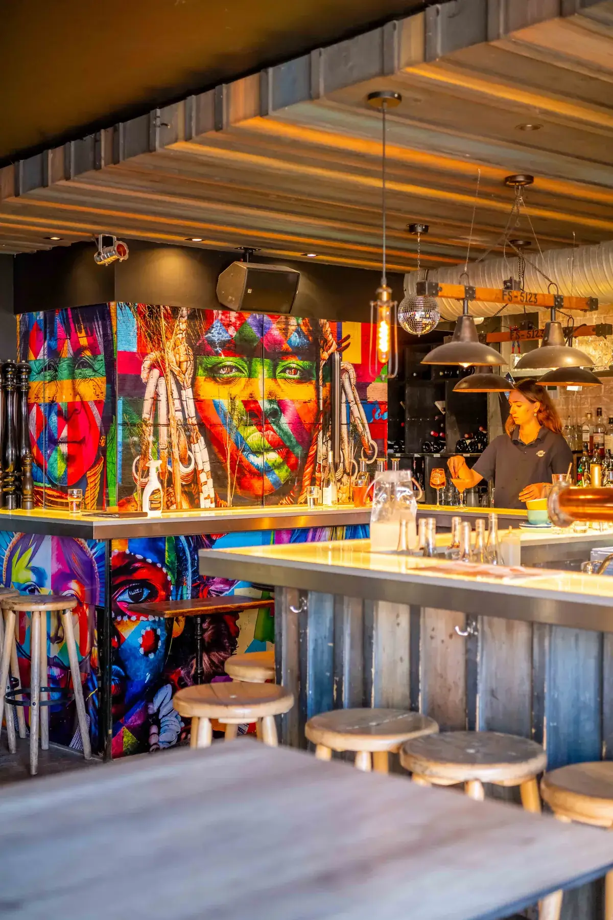 Bar de Chez Pont-Pont avec grande fresque colorée et serveuse derrière le comptoir
