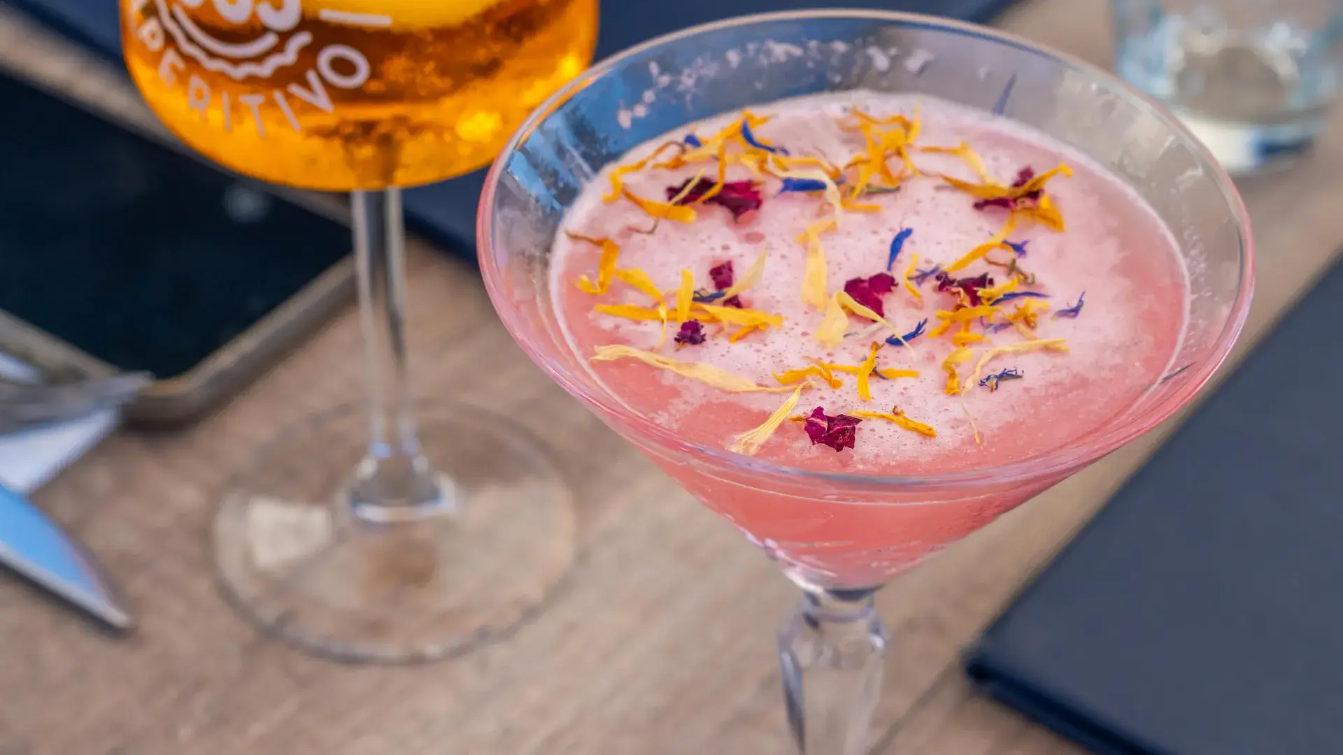 Cocktail rose aux pétales de fleurs posé sur la carte de Chez Pont-Pont