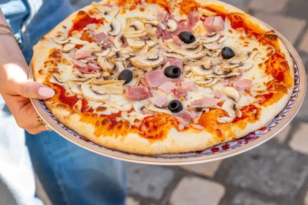 Pizza au jambon, champignons et olives portée à la main, restaurant Chez Pont-Pont