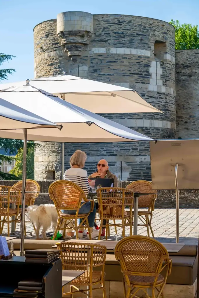 Clients attablés sous les parasols de la terrasse de Chez Pont-Pont, avec les tours du château d’Angers