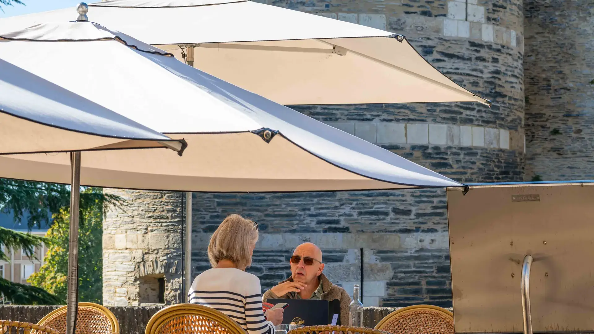 Clients attablés sous les parasols de la terrasse de Chez Pont-Pont, avec les tours du château d’Angers